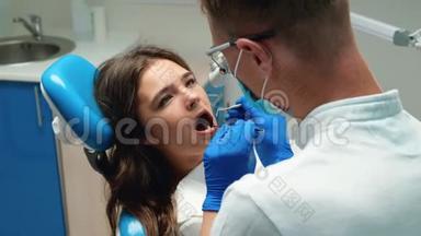 年轻的牙医<strong>戴</strong>着<strong>医用手套</strong>，<strong>戴</strong>着口罩，检查年轻的黑发女子`病人使用牙科器械的牙齿